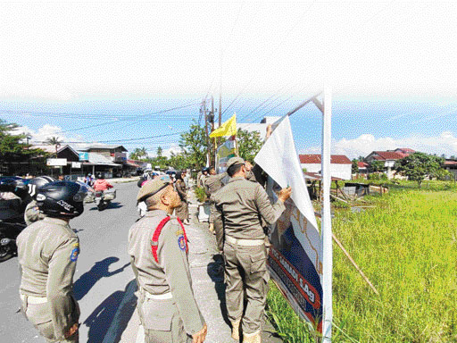 DITERTIBKAN: Petugas gabungan dari Bawaslu, Satpol PP Kota Payakumbuh, TNI dan Polri menertibkan sejumlah Alat Peraga Sosialisasi (APS) yang mengarah ke alat peraga kampaye di kawasan Jalan Pacuan, tepatnya di Simpang Pasar Ibuh, Kota Payakumbuh, Senin (2