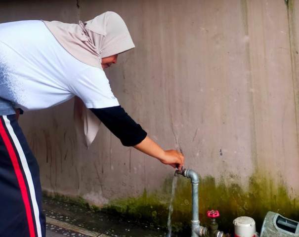 Yuni, pelanggan Perumda Air Minum Kota Padang di Kompleks Permata Surau Gadang (PSG) memutar kran yang sudah mengalir lancar airnya. Rabu sore (31/1).