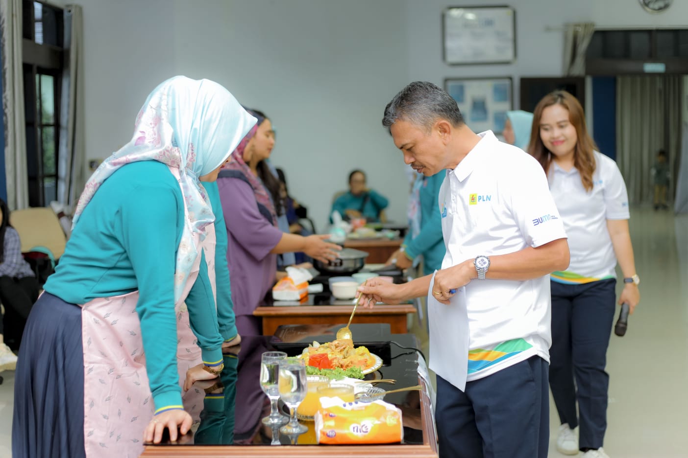 Manager PLN UP3 Bukit Barisan sedang mencicipi dan menilai hasil masakan peserta lomba memasak menggunakan kompor induksi.