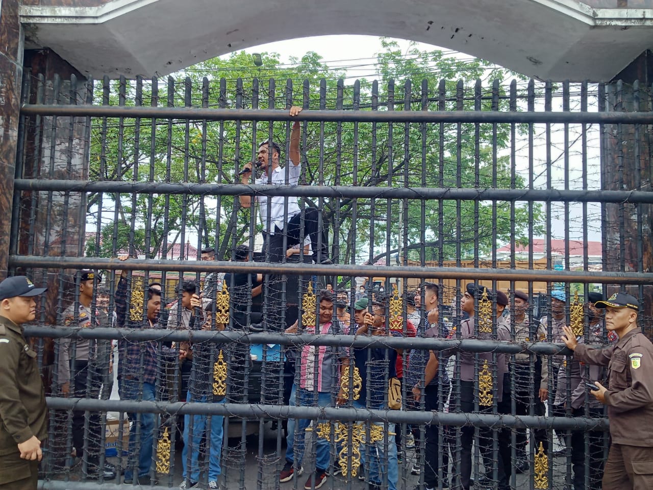 UNJUKRASA: Seorang pendemo memanjat pagar saat berunjuk rasa di Kantor Kejatisu, Selasa (13/8).(AGUSMAN/SUMUT POS)