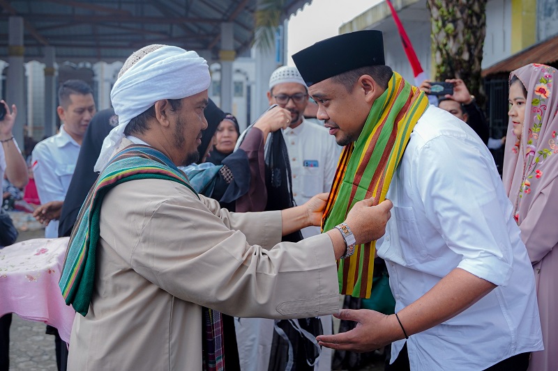 Pimpinan Al Yusufiyah H. Yusuf Amiril Soleh alias Tuan Guru Nalomok memakaikan kain kepada calon Gubernur Sumatera Utara nomor urut 1 Bobby Nasution , Sabtu (28/9/2024). (Ist)