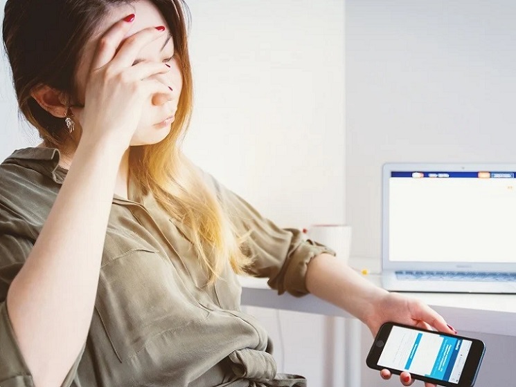 ilustrasi: Seorang wanita merasa kelelahan menatap layar hp dan laptop.