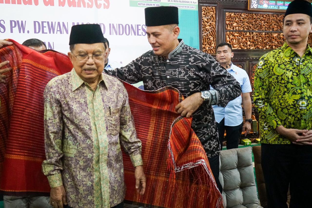 Ketua Majelis Mustasyar DMI Sumut Musa Rajekshah akrab disapa Ijeck menyematkan ulos kepada Ketua Umum DMI, (DMI) Jusuf Kalla di acara pelantikan pengurus Wilayah DMI Sumut di Masjid Al-Musannif.