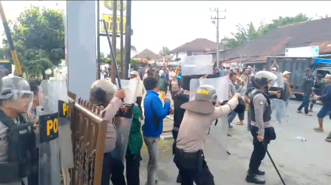 Petugas kepolisian Polres Dairi menggunakan tameng untuk melindungi diri dari aksi pelemparan batu yang dilakukan massa. (RUDY SITANGGANG/SUMUT POS)