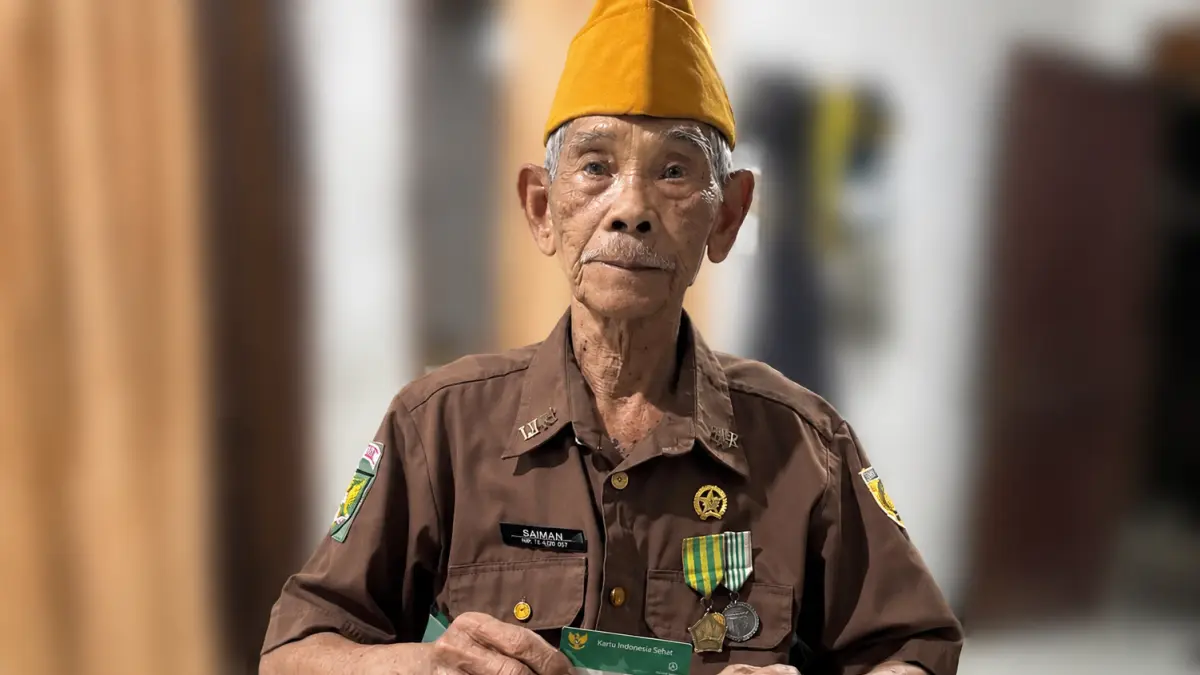 JKN: Saiman dengan mengenakan pakaian veteran sambil memegang kartu JKN miliknya.(FOTO: Laila Azizah).