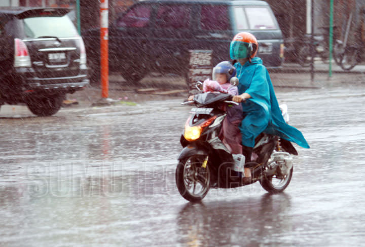 Foto: TRIADI WIBOWO/SUMUT POS Seorang ibu bersama putrinya menembus hujan deras dengan sepeda motor di jalan Sutomo Medan, Belum lama ini.