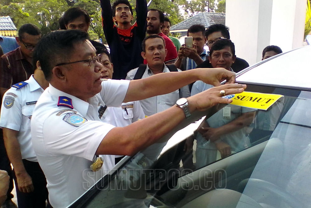 Foto: Sumut Pos Kadishub Sumut, Anthony Siahaan menempelkan stiker tanda khusus bertuliskan Sumut, ke mobil angkutan online, Senin (31/7). Stiker itu untuk Angkutan Sewa Khusus (ASK) yang sudah dinaungi perusahaan pemilik izin operasional.
