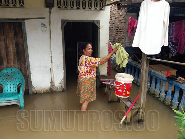 Seorang ibu menjemur pakaian dalam keadaan rumahnya direndam banjir, beberapa waktu lalu di Kabupaten Sergai.