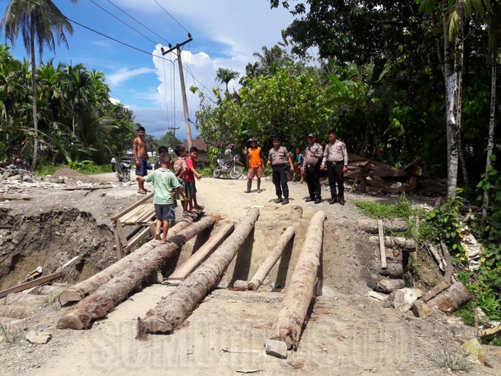 Foto: Famo/Sumut Pos Warga bersama personel Polsek Sirombu memperbaiki Jembatan Saono yang ambruk karena sering dilintasi truk-truk bernuatan lebih.
