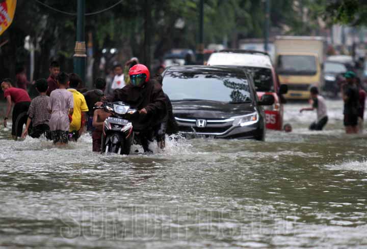 SUTAN SIREGAR/SUMUT POS BANJIR_Warga menggunakan kendaraan menembus banjir yang merendam Jalan dr Mansyur, Senin (9/7). Hujan deras yang mengguyur Kota Medan pada Minggu (8/7) malam ditambah meluapnya aliran anak Sungai Batuan menyebabkan puluhan rumah da