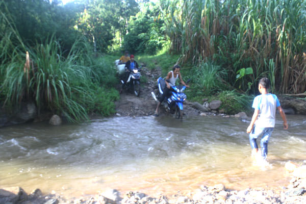 RUDY SITANGGANG/SUMUT POS  LEWATI SUNGAI: Warga Desa Alur Subur, Kecamatan Tanah Pinem, Kabupaten Dairi, harus melewati sungai beraliran deras guna menjual hasil tani ke Pasar Lau Baleng, Kabupaten Karo.