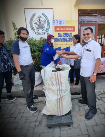 Camat Porsea Robert Manurung (kanan) mengikuti proses penimbangan sampah. Sementara Downstream Packaging Manager Danone Indonesia Annie Wahyuni memberikan sembako kepada mereka yang beli sembako bayar pake sampah.
