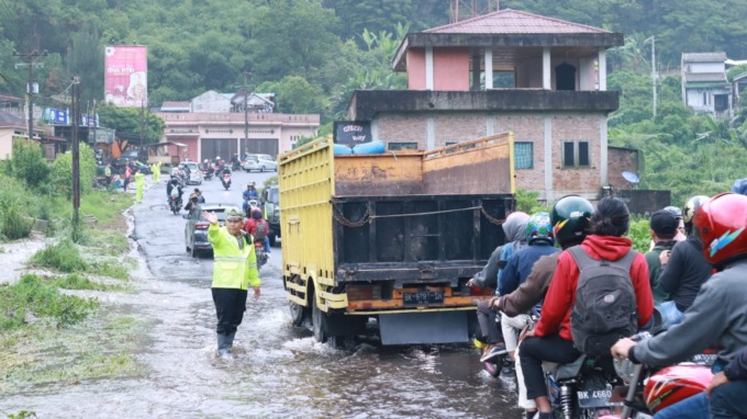 BANJIR: Petugas kepolisian mengatur lalu lintas saat banjir menggenangi ruas jalan Berastagi-Medan, Minggu (30/4). Sementara foto atas, seorang ibu dan anaknya duduk termenung setelah rumahnya disapu banjir bandang.DewI S LUIBIS/sumutpos.