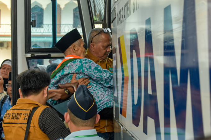 BANTU: Petugas membantu jamaah lansia menaiki bus untuk diberangkatkan dari Asrama Haji Medan menuju Bandara Kualanamu, Rabu (7/6) -MIFTAHUL HAYAT/JAWA POS.