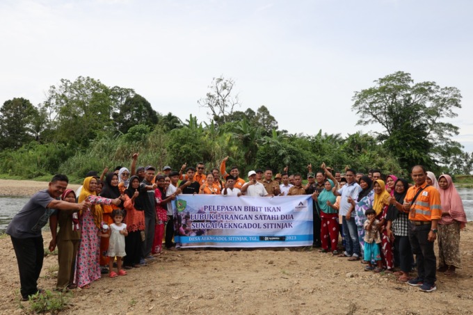 Senior Manager Community PT Agincourt Resources, Christine Pepah (belakang spanduk berseragam PTAR), bersama pihak Kecamatan Batangtoru dan masyarakat Aek Ngadol Sitinjak berfoto bersama usai melepas bibit ikan di lubuk larangan Sungai Aek Ngadol, Batangt