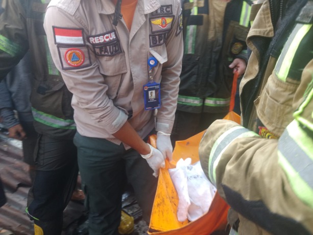 Petugas pemadam kebakaran dan polisi mengevakuasi jenazah korban dari dalam rumahnya yang terbakar, Selasa (27/2/2024).