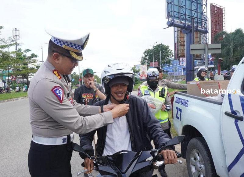 Dirlantas Polda Kepri, Kombes Tri Yulianto, memasangkan helm SNI kepada salah seorang pengendara sepeda motor.