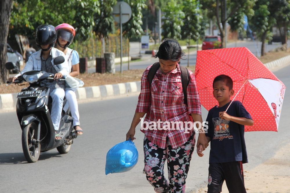 Seorang bocah berpayung karena cuaca panas di Batam.
