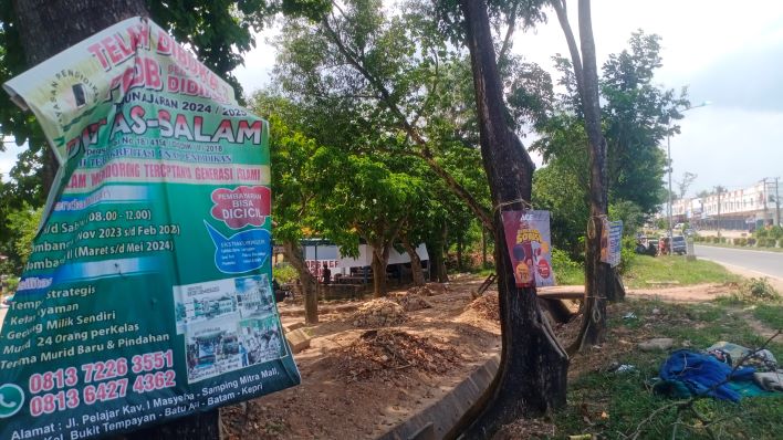 Plakat promosi yang ditempel menggunakan paku di pohon pinggir jalan.