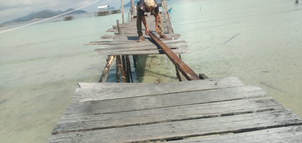 Seorang warga, Rikus menunjukkan tiang penyangga dan kayu pijakan Pelabuhan Kusik yang sudah lapuk.