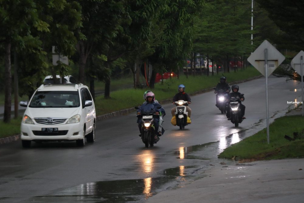 Pengendara sepeda motor mengenakan jas hujan untuk melindungi dari air hujan yang turun saat melintas di Jalan Raja Haji Kelana Batam Center, Minggu (18/5).