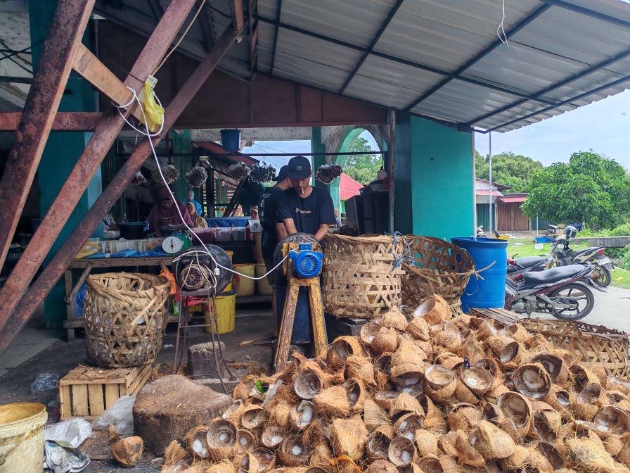 Penjual santan di pasar puan maimun sedang memarut kelapa.