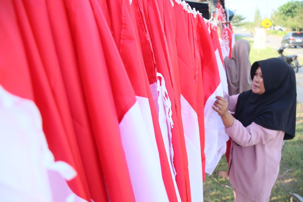 Seorang pedagang bendera, umbul Umbul dan akserosris yang bernuansa merah putih menyusun dagangan yang akan jual di kawasan Batam kota, Minggu (27/7).
