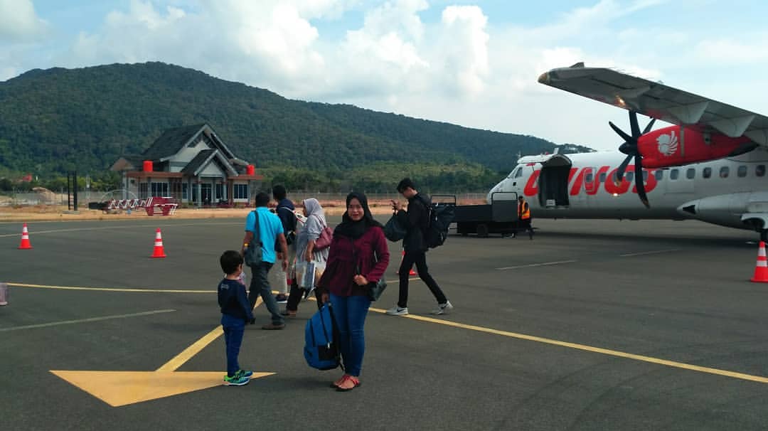 Salah satu penumpang sedang foto dengan latar belakang pesawat Wings Air di Bandara Letung. Mulai bulan depan, maskapai ini mengurangi jadwal penerbangan.