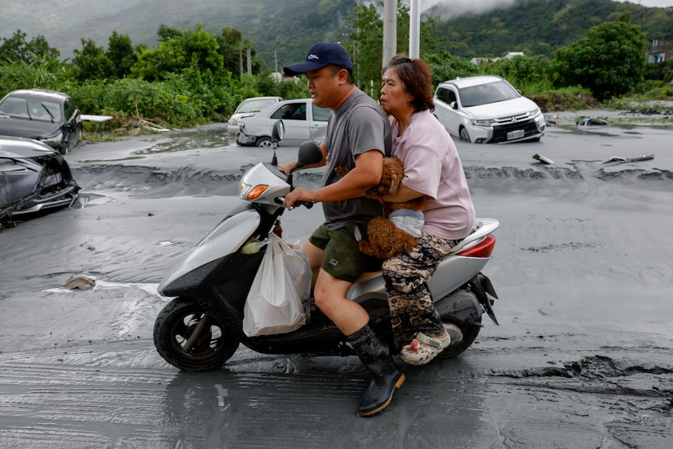 Pasangan mengendarai sepeda motor sambil membawa barang-barang dan seekor anjing peliharaan setelah banjir akibat Super Topan Ragasa di Hualien, Taiwan, Rabu (24/9/2025). F Ann Wang/Reuters