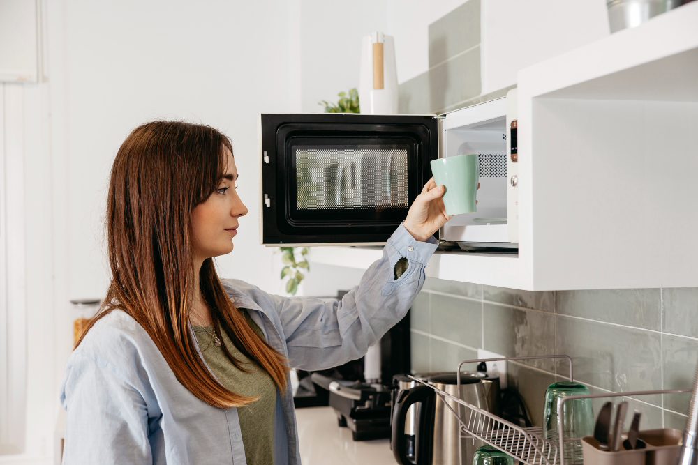 Ilustrasi seorang wanita memanaskan minuman ke microwave.
