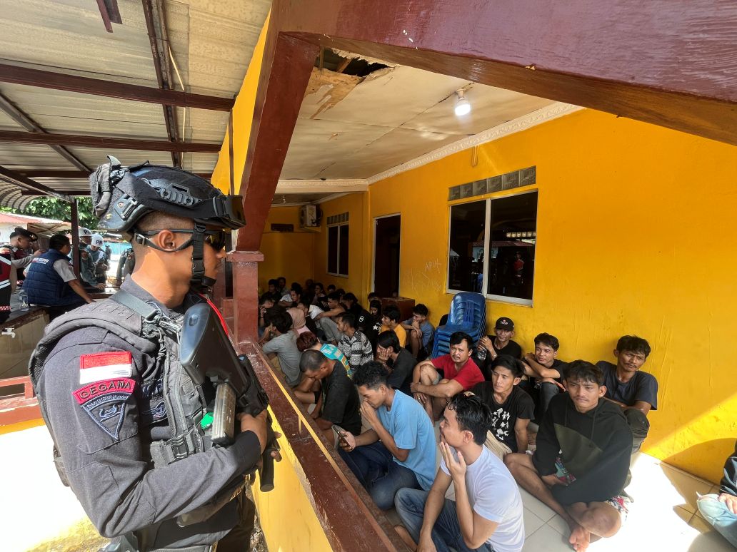 Warga yang diamankan saat penggerebekan narkoba di kampung Madani dijaga aparat.