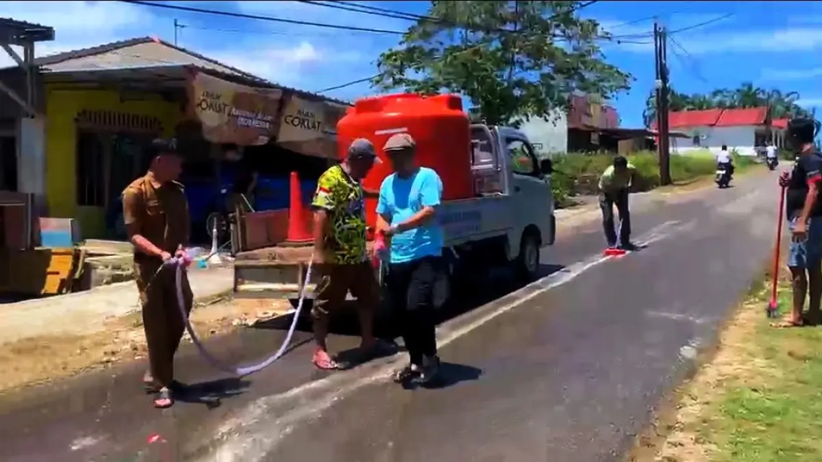 PEGAWAI Kantor Desa dan warga bergotong-royong membersihkan tumpahan oli di jalan Kampung Harapan, Desa Teluk Sasah, Kecamatan Seri Kuala Lobam, Senin (6/4/2026) siang. F.Suhairry Sembiring untuk Batam Pos