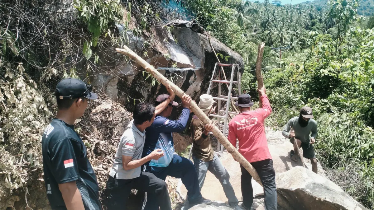 Camat Siantan Utara, Amiruddin (pakai topi) bersama warga merobohkan batu besar yang ancam keselamatan. F Ihsan Imaduddin/Batam Pos