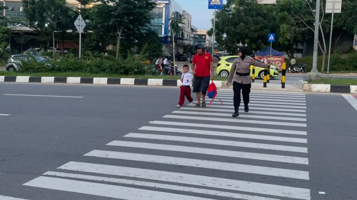 Personel Polwan Polresta Barelang membantu siswa menyeberang jalan dan mengatur arus lalu lintas di depan SD Negeri 001 Sungai Panas, Senin (27/7). (Istimewa)