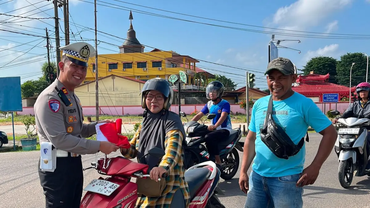 Petugas Satlantas Polres Bintan membagikan bendera Merah Putih kepada pengguna jalan di depan Taman Makam Pahlawan (TMP) Dwikora, Tanjunguban, Kecamatan Bintan Utara, Sabtu (1/8/2026). Kegiatan ini merupakan bagian dari semarak peringatan HUT ke-81 Kemerdekaan Republik Indonesia. F. Kiriman Yelvis untuk Batam Pos