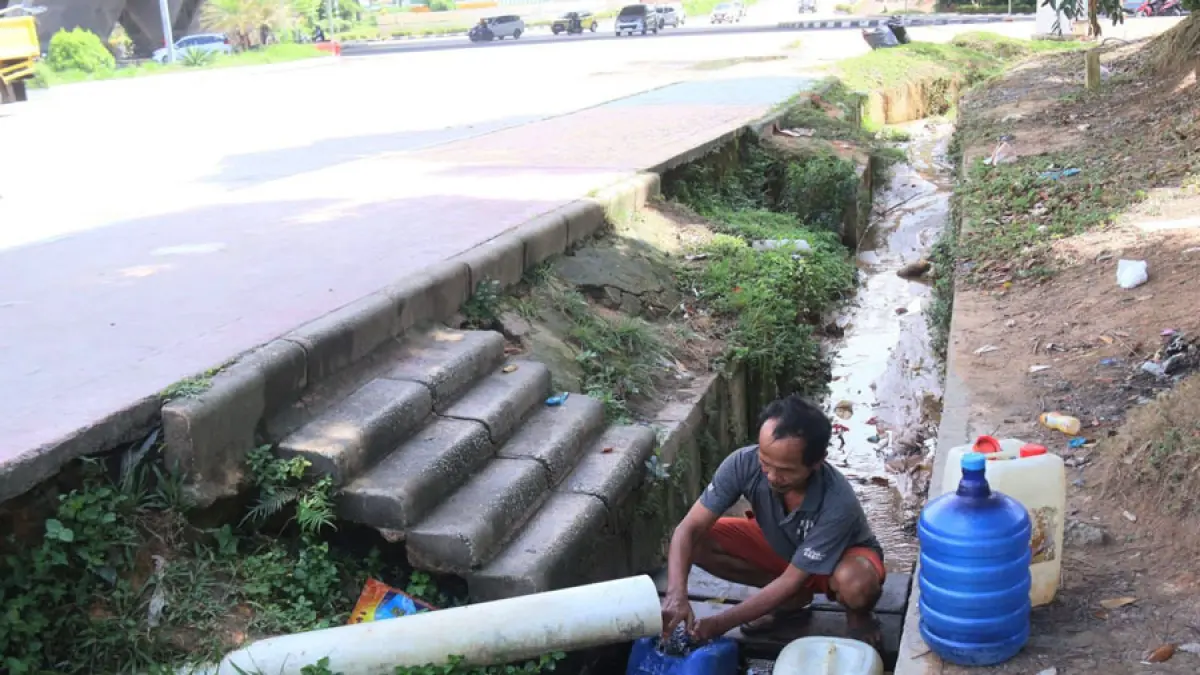 Warga mengambil air dari pipa di pinggir Jalan Simpang Jam atau Laluan Madani, Batam. F. Sya