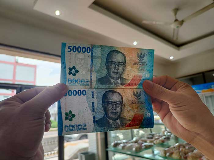 UANG PALSU : Karyawati toko kue di Jalan Ahmad Yani, Sampit memperlihatkan perbedaan uang asli (atas) dan uang palsu (bawah), beberapa waktu lalu.. (DOKUMEN/FAHRY/RADAR SAMPIT)