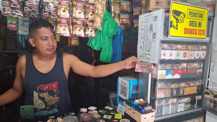 MERESAHKAN: Andri, pedagang warung kelontongan saat menunjukkan uang palsu yang ditemukan di tokonya, Kamis (19/6/2025). //Foto.FAHRY/RADAR SAMPIT