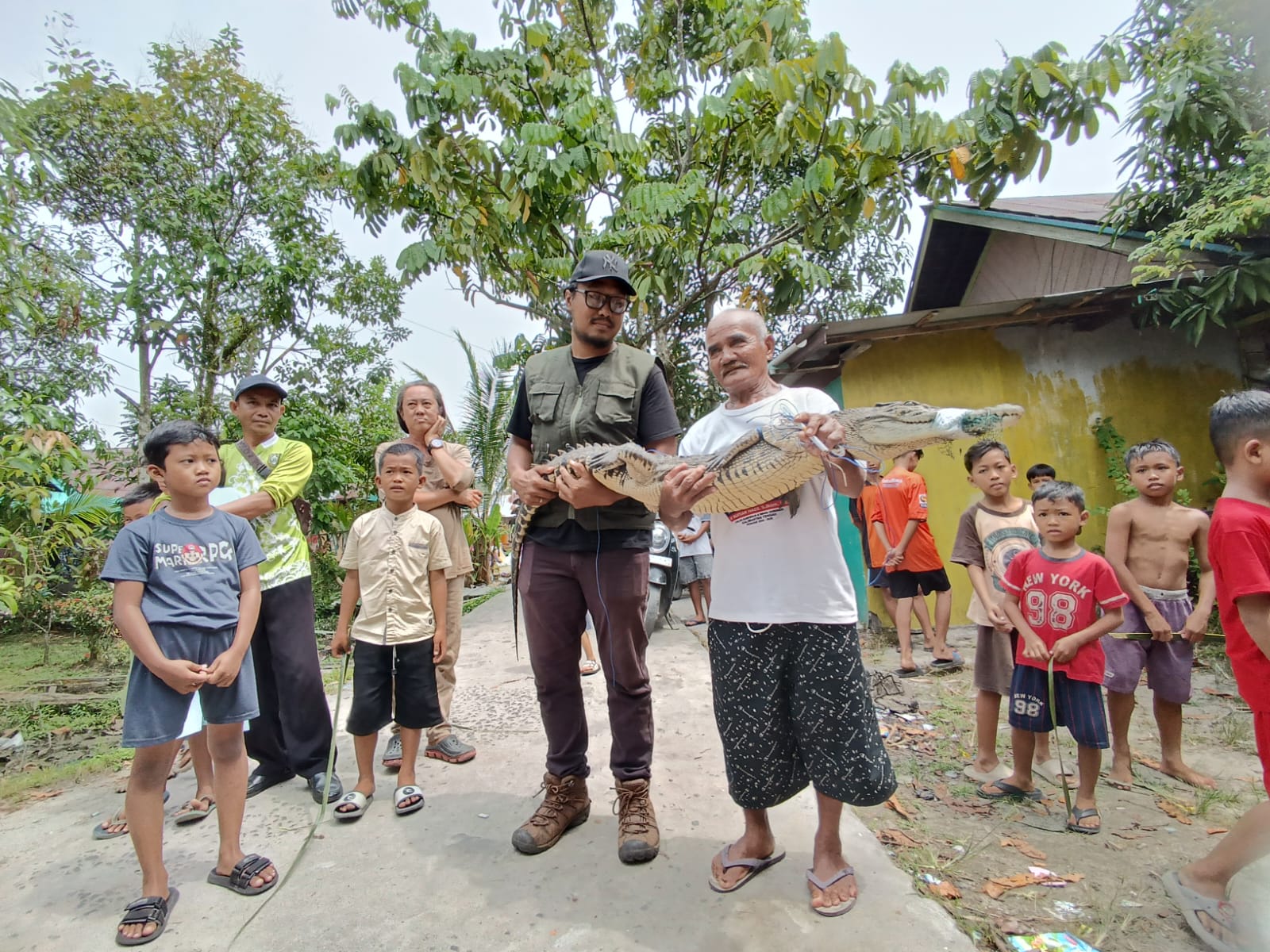 Marliansyah (kaus putih) bersama Aktivis Pecinta Satwa Liar Harry Siswanto, mengangkat buaya, sebelum diamankan dari lokasi di Jalan Iskandar 25 Sampit, Jumat (27/3/2026). (Usay/Radar Sampit)