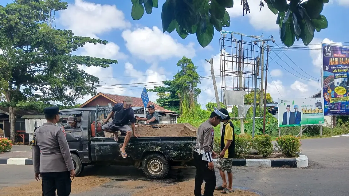 Personel Polres Seruyan menaburkan pasir untuk menyerap minyak di Bundara I Kuala Pembuang agar jalan kembali aman dilalui kendaraan. (RIFANI/RADAR SAMPIT)