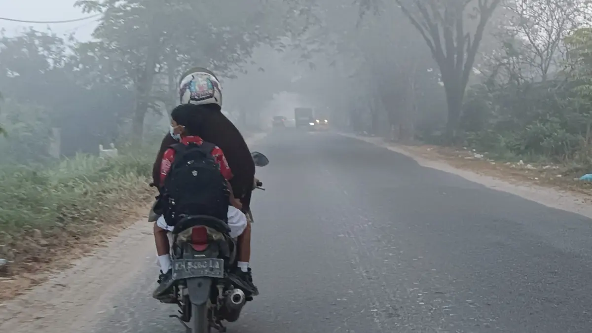 Seorang anak berangkat sekolah diantar orang tuanya, menembus kabut asap akibat kebakaran lahan yang menyelimuti Sampit, Kabupaten Kotawaringin Timur, Rabu pagi (5/8/2026). (Usay Nor Rahmad/Radar Sampit)&nbsp;