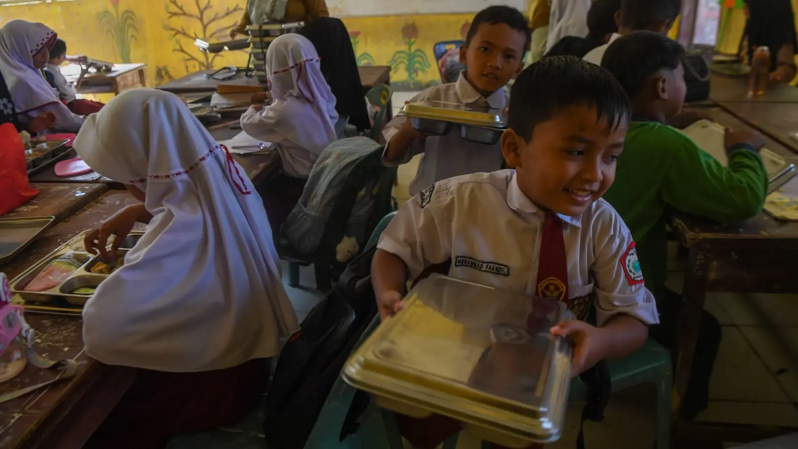 SENYUM BAHAGIA: Siswa SD Negeri 1 Tualang Cut membawa ompreng berisi menu makanan bergizi gratis (MBG) di Manyak Payed, Kabupaten Aceh Tamiang. (NOVA WAHYUDI UNTUK BP)