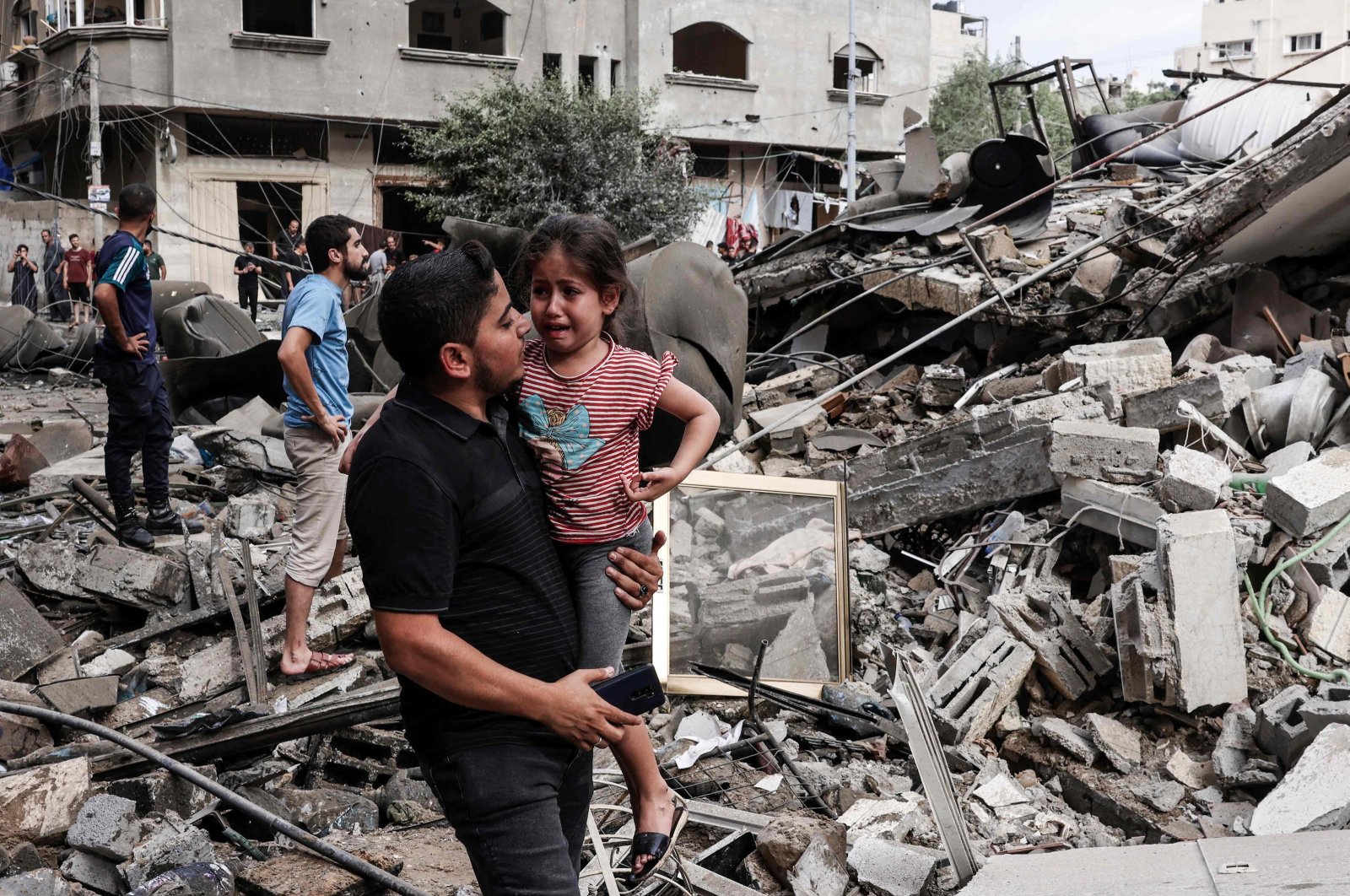 Seorang pria menggendong seorang anak yang menangis saat dia berjalan di depan sebuah bangunan yang hancur akibat serangan udara Israel di Kota Gaza pada 7 Oktober 2023. (Foto AFP)