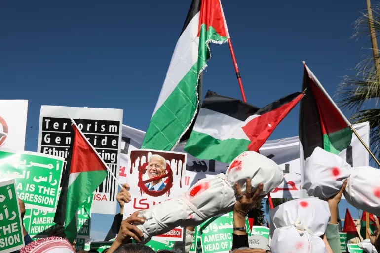Orang-orang memegang tubuh palsu yang dibungkus kain selama protes mendukung warga Palestina di Gaza di Amman, Yordania, pada 8 Desember 2023 (Alaa Al Sukhni/Reuters)