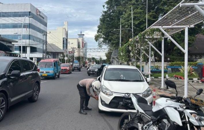 PETUGAS menggembosi ban mobil yang parkir sembarangan.
