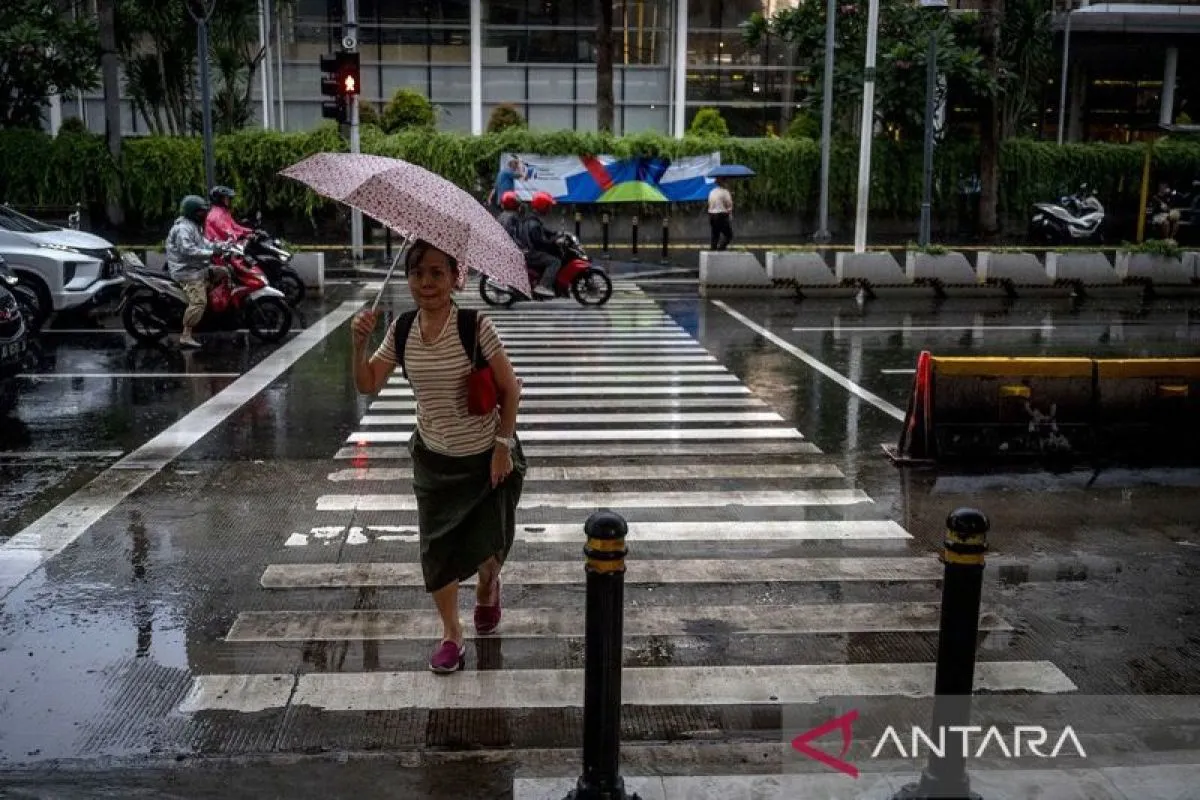 Seorang warga menggunakan payung saat turun hujan di kawasan Bundaran HI, Jakarta