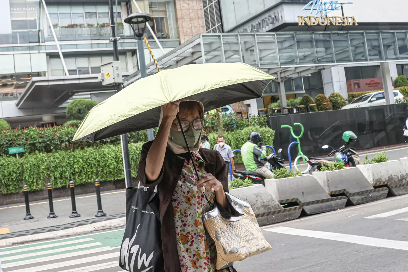 Pejalan kaki menggunakan payung dan jaket untuk melindungi dari panas di sekitar Bundaran HI, Jakarta, Selasa (14/10/2025). (Hanung Hambara/Jawa Pos)