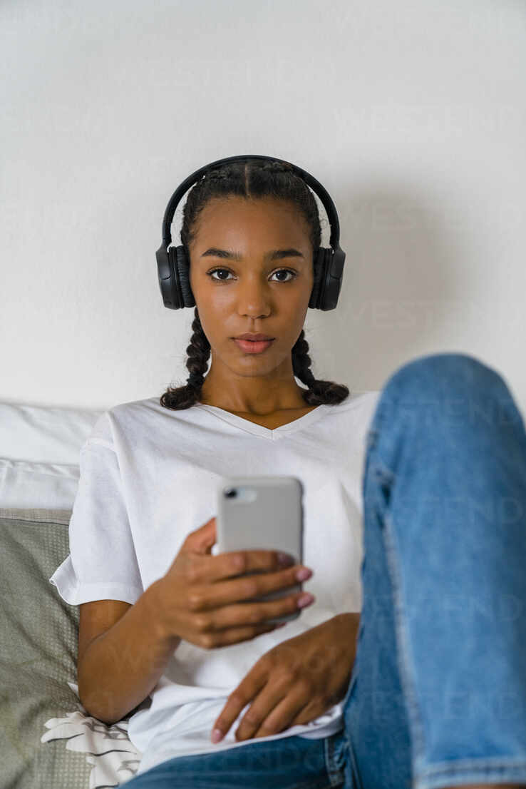 Young teenage girl listening to music through headphone on smart phone at home