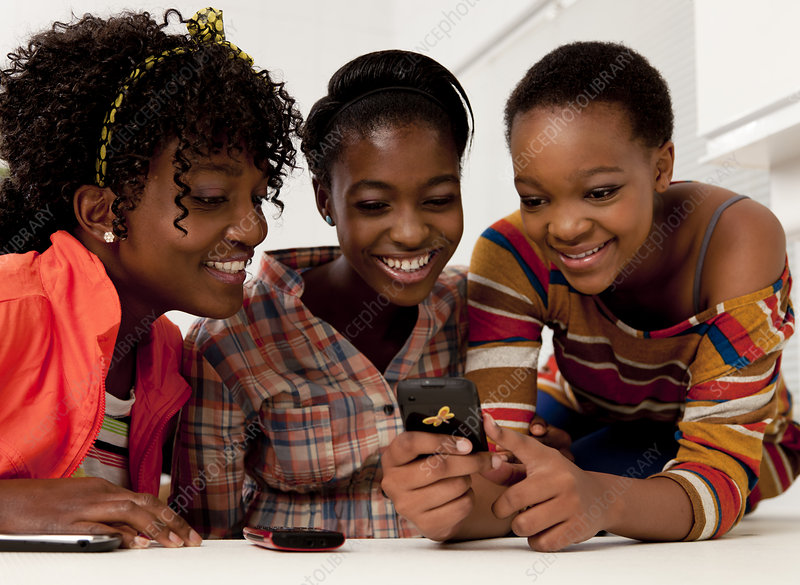 Three teenage girls sitting indoors, looking at their mobile phones.