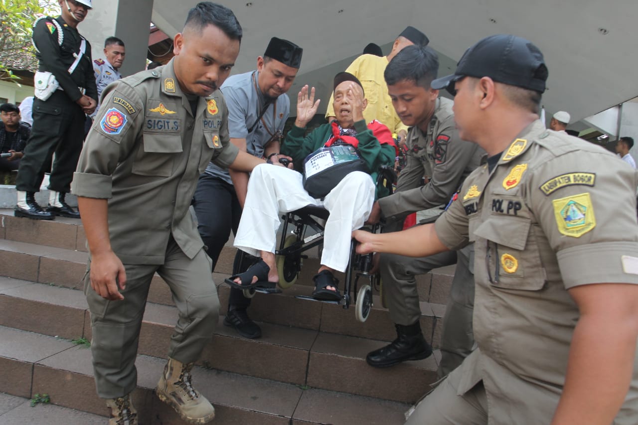 Petugas Satpol PP Kabupaten Bogor, membantu jamaah haji yang siap diberangkatkan ke tanah suci, Minggu (12/5/2024).